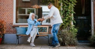 Jonge buurman geeft zijn oudere buurvrouw een kopje koffie buiten op een bankje in de straat