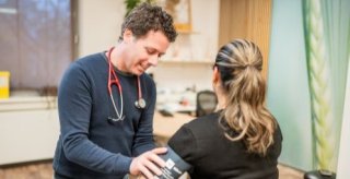 Huisarts doet bloeddrukmeter om bij patiënt. 