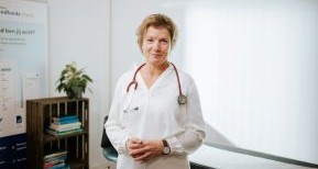 Een vrouwelijke huisarts in haar praktijk kijkt vriendelijk in de camera