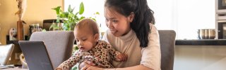 Vrouw thuis achter een laptop en baby op schoot
